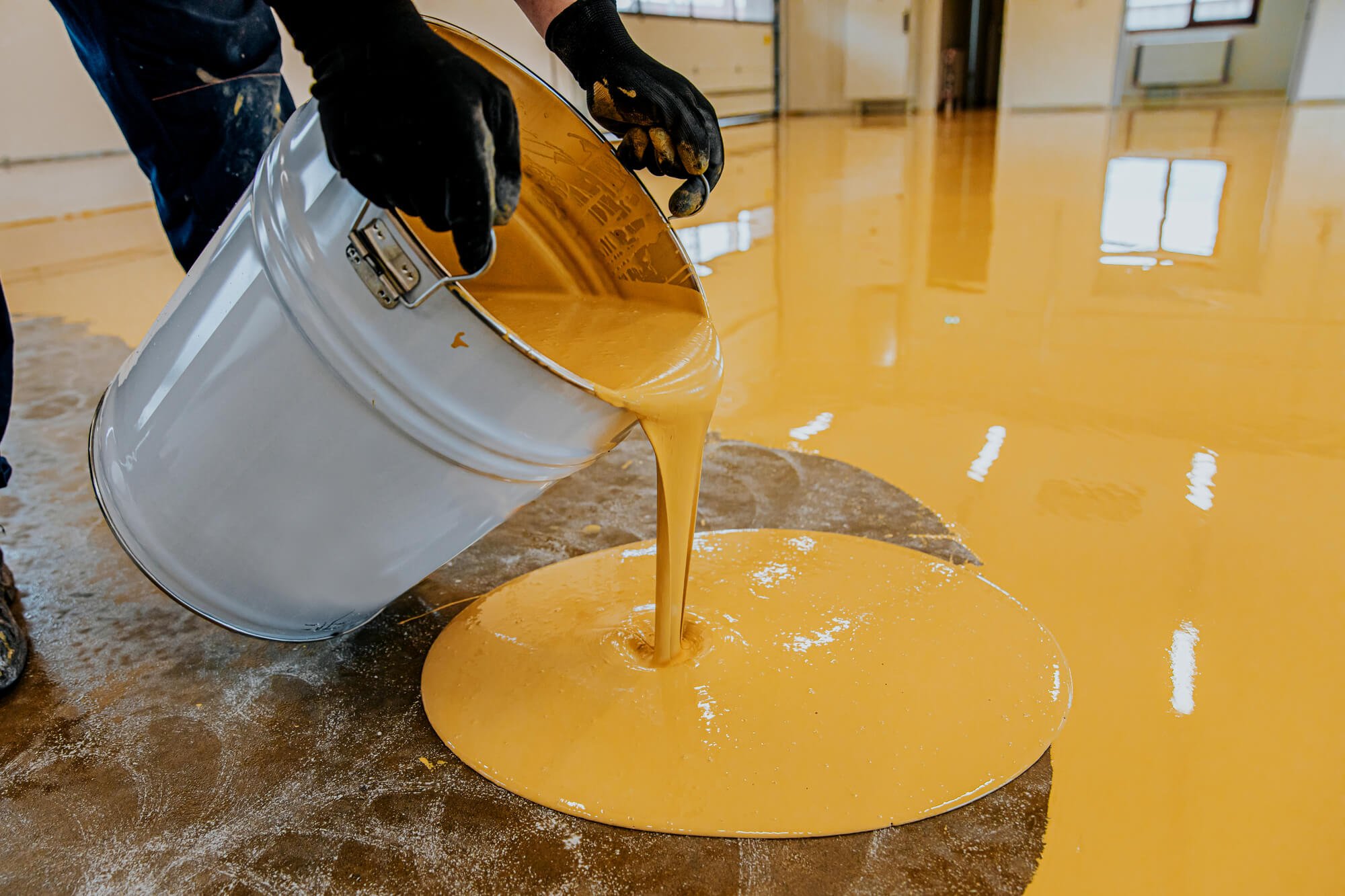 A man pouring yellow epoxy resin on a floor