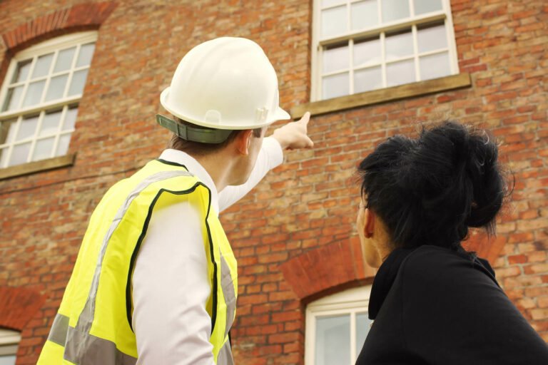 A builder with white hard helmet next to a lady is pointing to a house