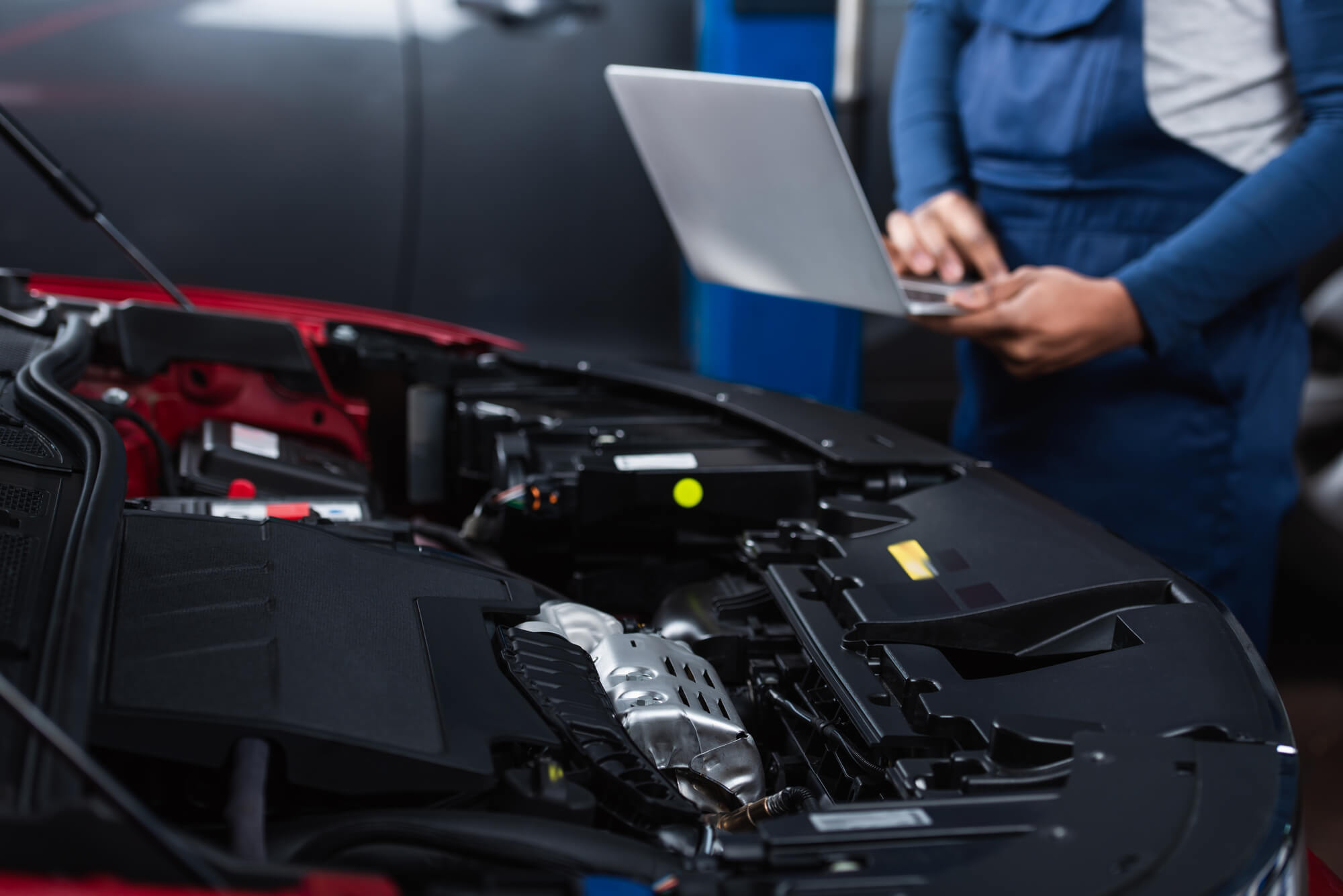 Mobile car technician by the front engine holding a laptop.
